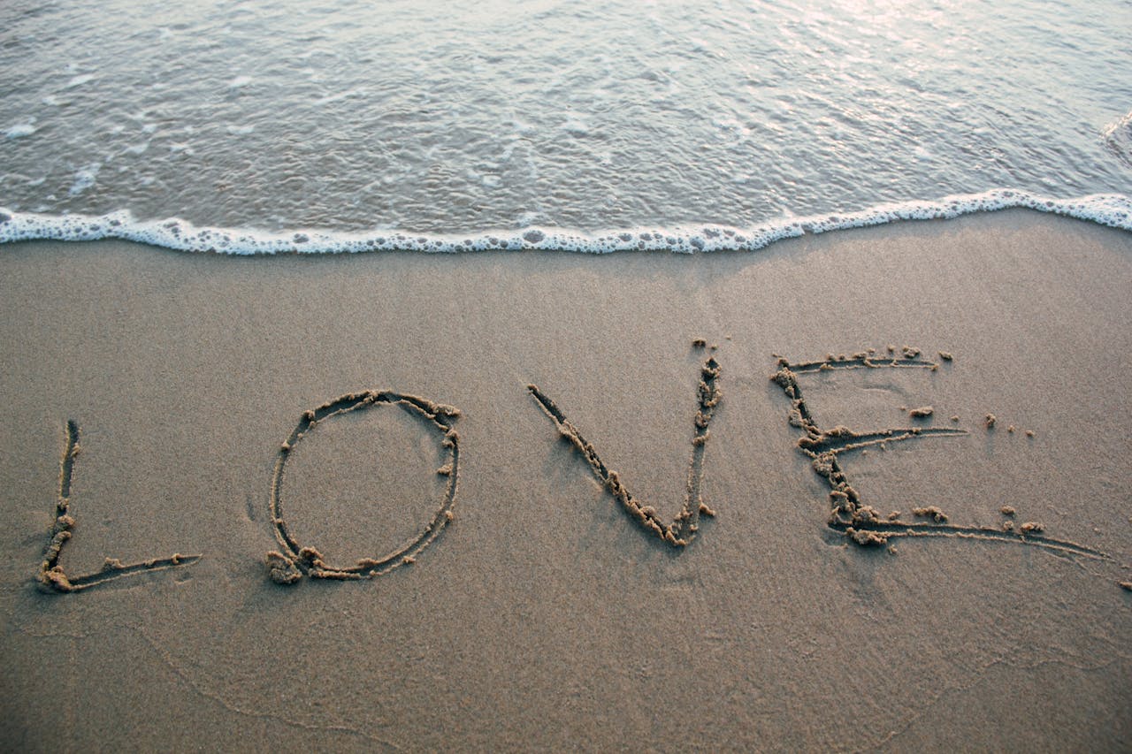 Love written in sand with ocean waves at the beach, evoking romance and tranquility.